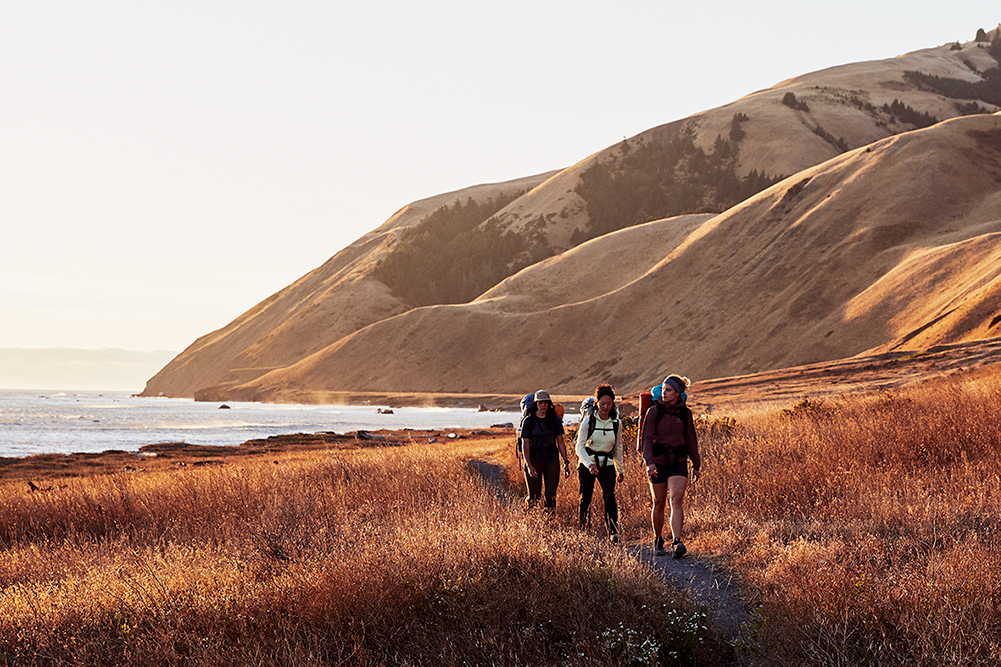 Three women are hiking along a scenic coastline