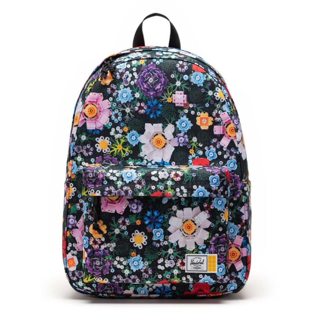 colourful LEGO floral pattern Herschel backpack with a front zip pocket, a black top carry handle and a white Herschel logo label at the bottom-right front pocket