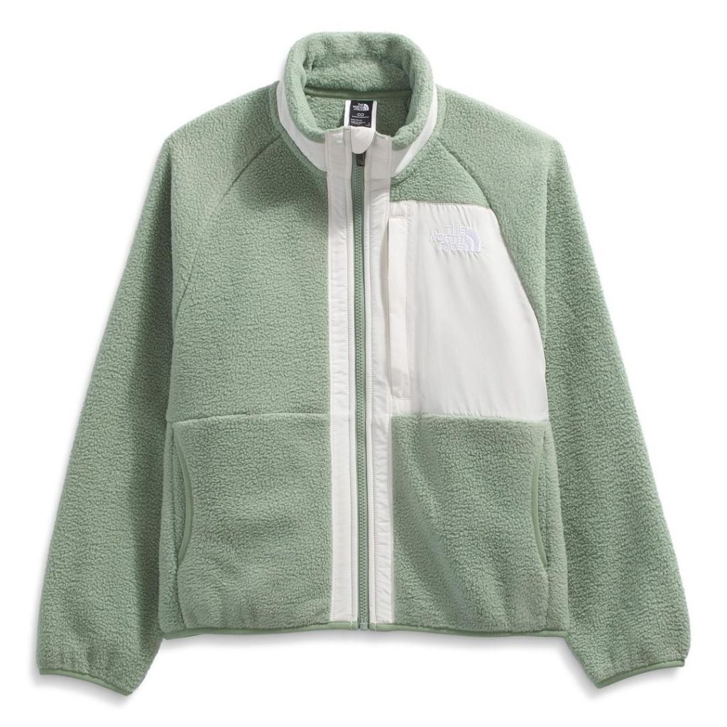 sage green The North Face fleece full-zip jacket with contrast white trim along the front zipper and contrast white panel pocket at the left chest with white The North Face embroidered logo; stretchy sage elastic banding at cuffs and hem, stand collar with contrast white chin guard and contrast stripe along collar